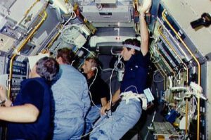 Členové výpravy STS-9 shromáždění okolo monitoru v laboratoři Spacelab. Ulf Merbold je úplně vpravo.