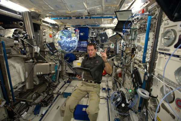 Čtení z knihy „Čas na příběh z kosmu“ od Jeffrey O. Bennetta pro děti na Zemi – jsem na ISS a za mnou se vznáší glóbus.