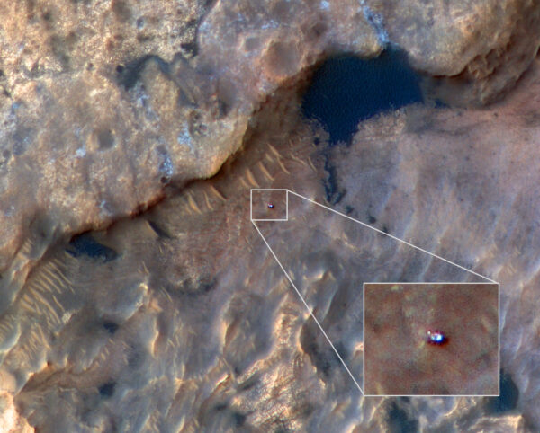 Curiosity z MRO 31. 5. 2019. Světlá skvrnka vlevo od těla robota je hlava s kamerami na stožáru. Kol se jeví jako šestice tmavých plošek podél těla robota. Zdroj: mars.nasa.gov