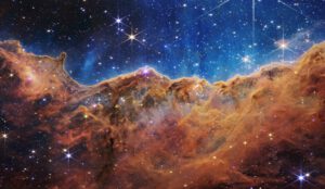 Část obří mlhoviny Carina na snímku kamery NIRCam JWST. Oblast přezdívaná Vesmírný útes je rozhraním mezi oblastí erodovanou silným ultrafialovým zářením horkých hvězd nahoře (mimo snímek) a chladnějších molekulárních oblak s intenzivní tvorbou hvězd. Zdroj: esawebb.org