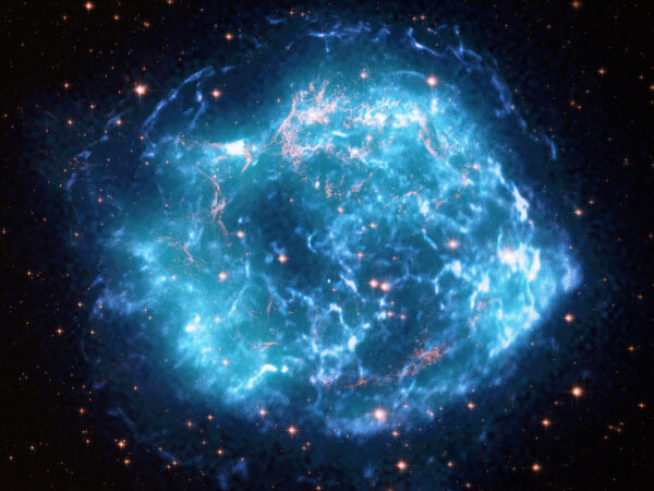 Složený snímek pozůstatku supernovy Cas A. Modrá barvap ředstavuje data z teleskopu Chandra. Tyrkysovou modř mají data z IXPE a zlatě jsou zvýrazněna data z Hubbleova teleskopu.