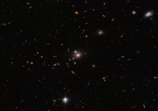 Zhruba uprostřed obrázku, kousek od naoranžovělé galaxie vidíte dva jasné namodralé objekty připomínající hvězdu. Nejde ovšem o skutečné hvězdy, nýbrž o kvasar. Původně se mělo za to, že jsou to dva objekty. Brzy se ale zjistilo, že jde o dva obrazy téhož objektu, kvasaru Q0957+561. Jde o vůbec první zaznamenanou gravitační čočku. Tento snímek je z Hubbleova dalekohledu.