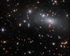 Kupa galaxií RX J2129 a na pozadí červené vzdálené čočkované objekty. 