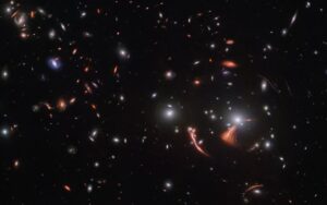 Kupa galaxií SDSS J1226+2149 s čočkovanými objekty ve svém okolí. Kousek vpravo dole od středu snímku vidíme kosmického mořského koníka, galaxii protaženou do tvaru jakéhosi nakloněného písmene Y.