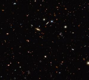 Totožný snímek jako výše. Tentokrát ovšem s bílými kolečky, která označují kvasar a jednotlivé k němu náležející galaxie (v některých kolečcích je po dvou galaxiích). 