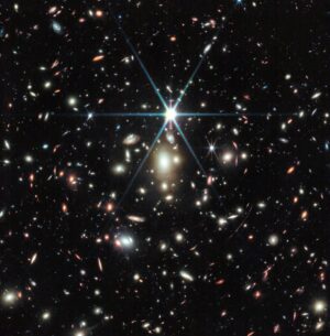 Kupa galaxií WHL0137-08 na snímku z Vesmírného dalekohledu Jamese Webba, přesněji z přístroje NIRCam. Na první pohled zaujme velmí jasná a výrazná hvězda s typickými osmi difrakčními hroty. Ta patří do Mléčné dráhy, podobně jako několik dalších hvězd na obrázku. Pozorné oko si povšimne deformovaného obrazu galaxie Sunrise Arc a hvězdy Earendil. Není to ovšem zdaleka jediný projev gravitačního čočkování na této fotografii.
