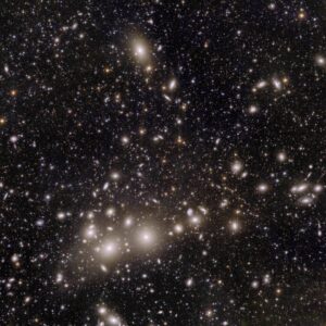 Kupa galaxií v Perseovi (k ní patří ty jasnější, větší a světlejší galaxie). Na pozadí pak další desetitisíce vzdálenějších galaxií.