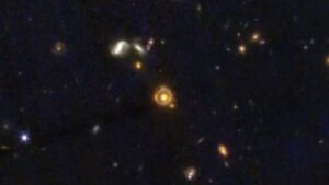 Oddálený pohled na Einsteinův prstenec JWST-ER1, takže je vidět i širší okolí.
