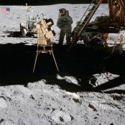 Astronaut Apolla 16 John Young je vyfotografován na povrchu Měsíce s pozlacenou kamerou/spektrografem pro daleké ultrafialové záření George Carrutherse, první observatoří na Měsíci. Lunární modul „Orion“ je vpravo a lunární vozítko je zaparkováno v pozadí vedle americké vlajky.