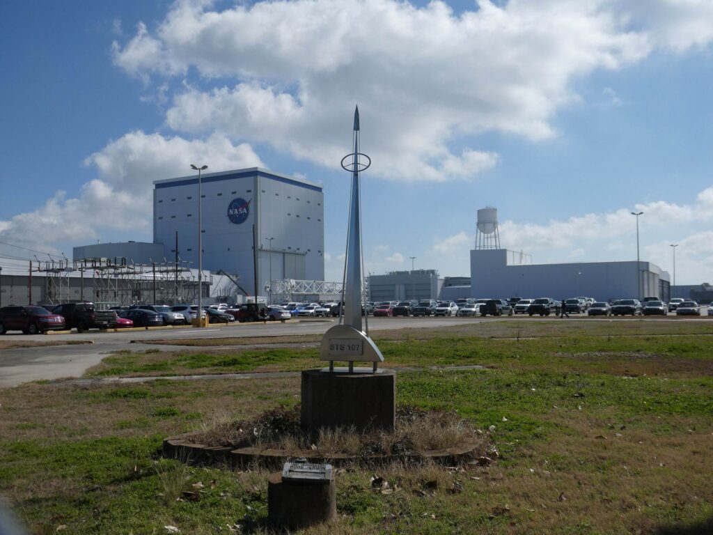 Pohled na továrnu Michoud Assembly Facility, vpřed pak pomníčekpřipomínající nešťastnou misi raketoplánu Columbia STS-107