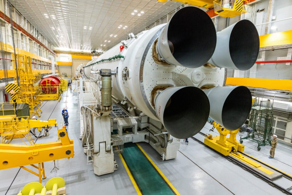 Raketa Sojuz-5 je umístěna na transportním zařízení v montážní hale, kde probíhá kontrola, testování a příprava před přesunem na startovní rampu. Okolní konstrukce, jeřáby a technici ukazují skutečné měřítko – jde o velmi robustní nosič navržený pro vynášení těžších nákladů na oběžnou dráhu. Foto: Roskosmos