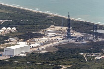 Letecký pohled na startovní komplex 36 na kosmodromu Cape Canaveral Space Force Station, zachycující následky exploze rakety New Glenn z noci na minulý pátek. Samotná raketa se při výbuchu prakticky rozpadla a zanechala po sobě trosky transportéru a montážního zařízení na betonové ploše. Vpravo od rampy jsou viditelné znetvořené zbytky bleskosvodu. Velký hangár pro zpracování (vlevo) výbuchem prošel bez větších škod, stejně jako nádrže na pohonné látky a distribuční systémy.