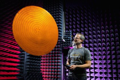 Matt Bray, hlavní designér antén pro Dragonfly, kontroluje vysokoziskovou anténu (HGA) sondy Dragonfly v testovací komoře Johns Hopkins Applied Physics Laboratory v Laurel v Marylandu. Anténa HGA je radiální štěrbinová anténa, která využívá mnoho malých štěrbin, které společně vytvářejí úzký, soustředěný rádiový svazek. Hroty v pozadí jsou speciální absorbéry, které pohlcují rozptýlené rádiové vlny, díky čemuž se prostor chová spíše jako otevřený (kosmický) prostor.